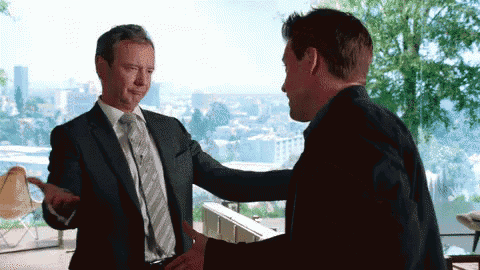 two men in suits and ties are shaking hands in front of a window