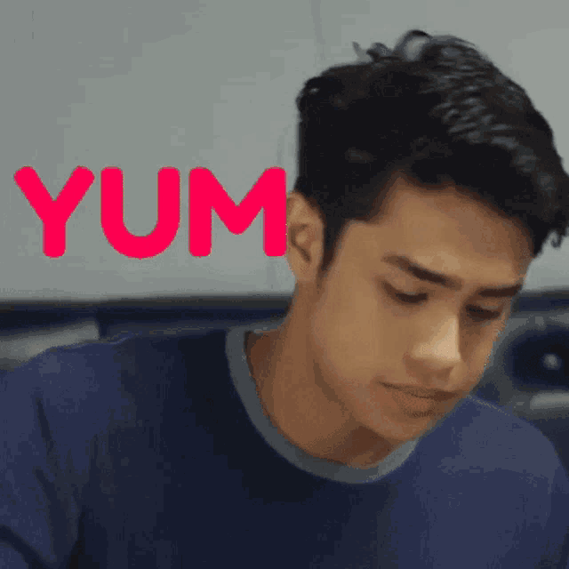a young man in a blue shirt with the word yum in red behind him