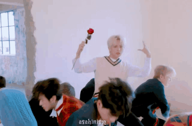 a group of young men are dancing in a room while a man holds a rose .