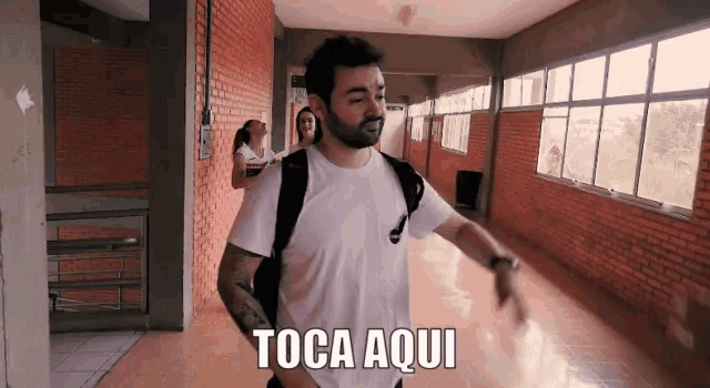 a man in a white shirt is walking down a hallway with the words toca aqui written on the floor