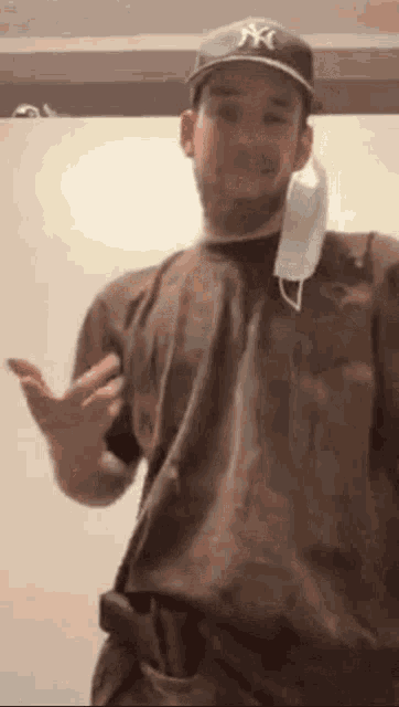 a man wearing a hat and a face mask is standing in front of a white wall .