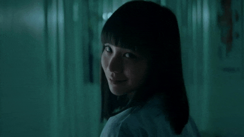 a woman in a white shirt is standing in a dark hallway and smiling at the camera .