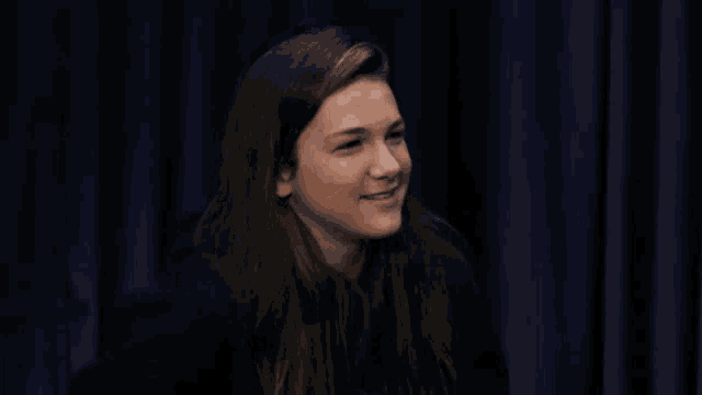 a woman in front of a blue curtain smiles