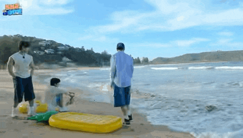 a group of people are standing on a beach with a yellow raft in the water .