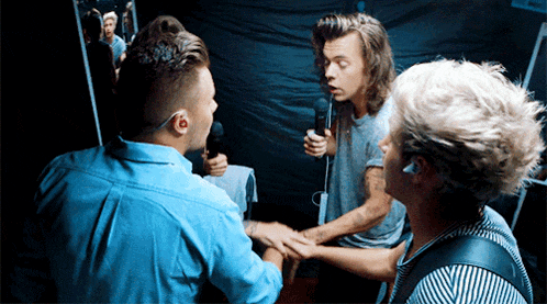 a man in a denim shirt holds a microphone while talking to two other men