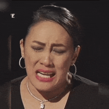 a woman wearing hoop earrings and a necklace is crying with the letter e above her