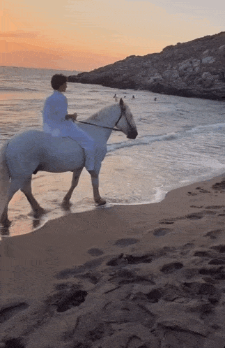 a person is riding a white horse on a beach