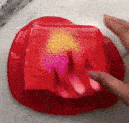 a person is playing with a red jelly with pink and yellow glitter .