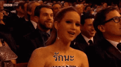 a woman in a strapless dress is blowing a kiss while sitting in a crowd .