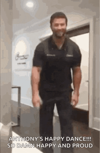 a man in a black shirt is standing in a hallway holding a bottle of beer .