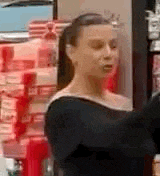 a woman is standing in front of a shelf in a store looking at something .
