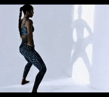 a woman is dancing in front of a mirror with a shadow of a man on the wall behind her .