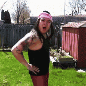 a woman wearing a pink headband and a black tank top is standing in a yard