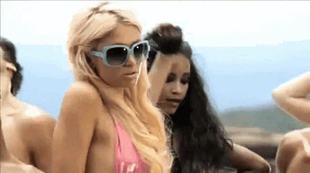 a woman in a pink bikini and sunglasses is standing in a crowd of people