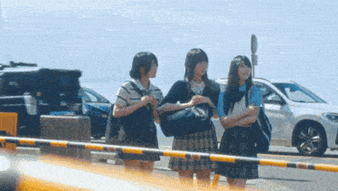 three girls standing in front of a barrier with a car in the background