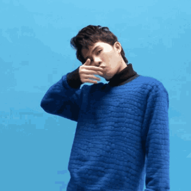 a man wearing a blue sweater covering his mouth with his hand