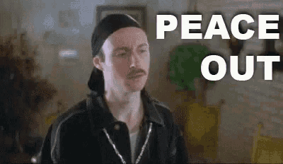 a man with a mustache is sitting in a living room with the words `` peace out '' written on the screen .