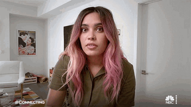 a woman with pink hair is sitting in a living room with a nbc logo behind her
