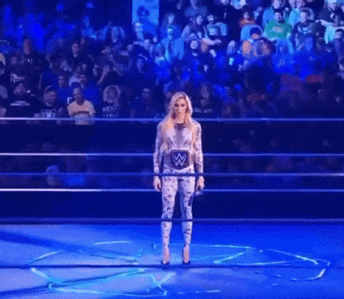 a woman is standing in a wrestling ring with a w logo on her chest