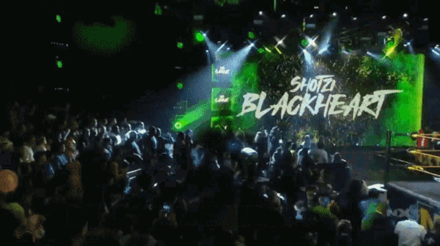 a crowd of people are gathered in front of a large screen that says shotz blackheart