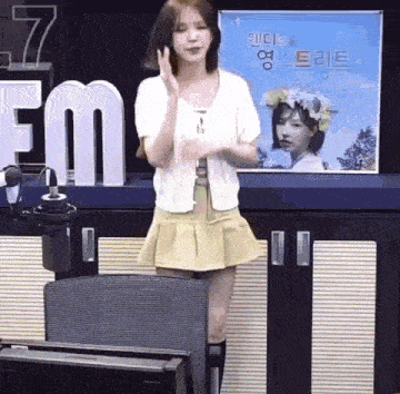 a woman in a yellow skirt is standing in front of a microphone in a radio studio .