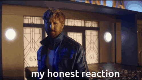 a man in a blue jacket stands in front of a building with the words my honest reaction below him