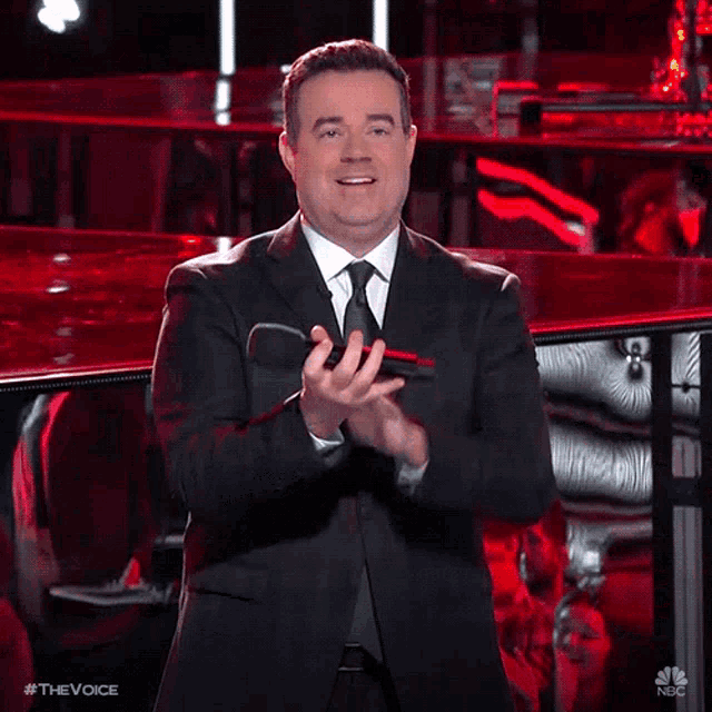 a man in a suit and tie applauds while holding a microphone