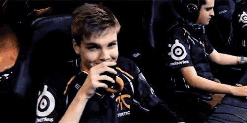 a man wearing a black shirt that says fnatic drinks from a cup