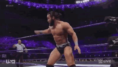 a wrestling match is being held in a stadium and a referee is standing behind the wrestlers .