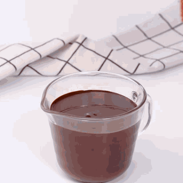 a measuring cup filled with chocolate sauce next to a napkin