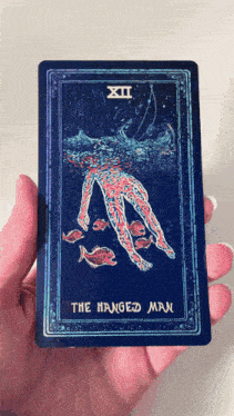 a person is holding a tarot card that says the hanged man on it