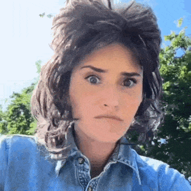 a woman wearing a denim shirt and a wig is making a face .