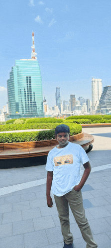 a young man stands in front of a city skyline wearing a white t-shirt with a picture of a house on it