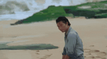 a man is sitting on a sandy beach looking at the ocean .