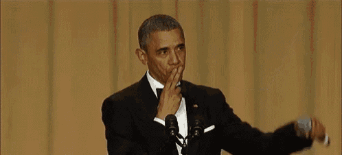 barack obama is giving a speech in front of a microphone and covering his mouth .