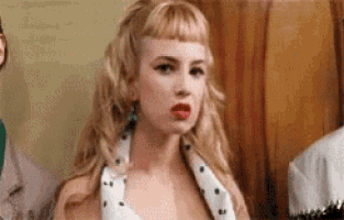 a woman with blonde hair and red lipstick is wearing a white dress with polka dots and a scarf around her neck .