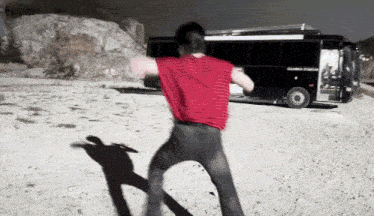 a man in a red shirt is dancing in front of a bus that says columbia