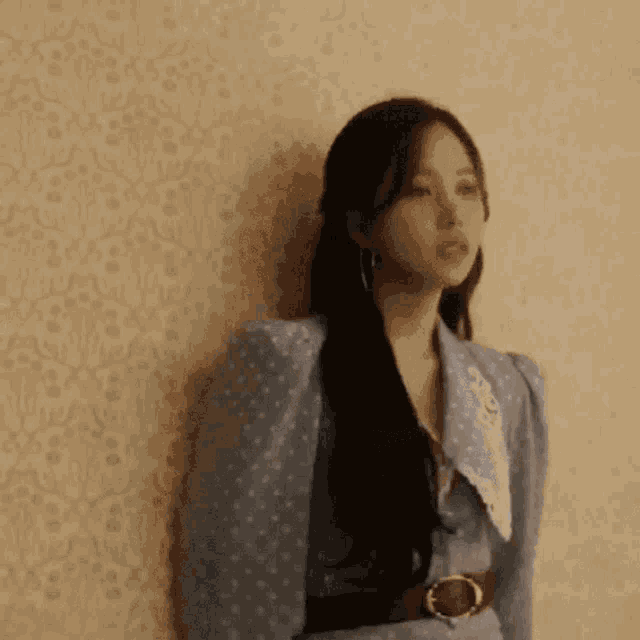 a woman in a blue dress is leaning against a wall and looking at the camera .