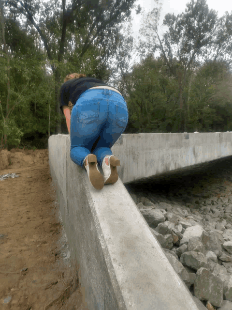 a woman in blue jeans and white boots is standing on a concrete wall