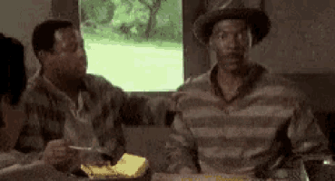 a group of men are sitting at a table eating food . one of the men is wearing a hat .