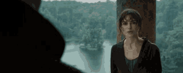 a woman is standing next to a man in front of a lake in a forest .