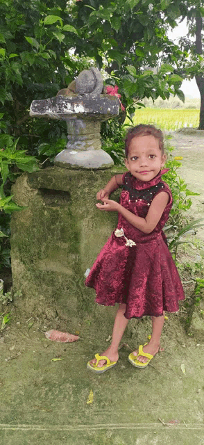 a little girl in a red dress and yellow flip flops is standing in front of a statue