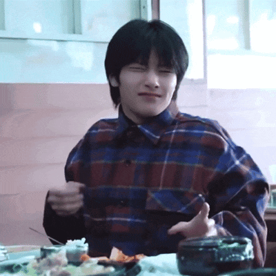a young man in a plaid shirt is sitting at a table with a plate of food .