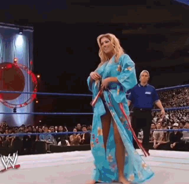 a woman in a blue kimono is walking in a wrestling ring