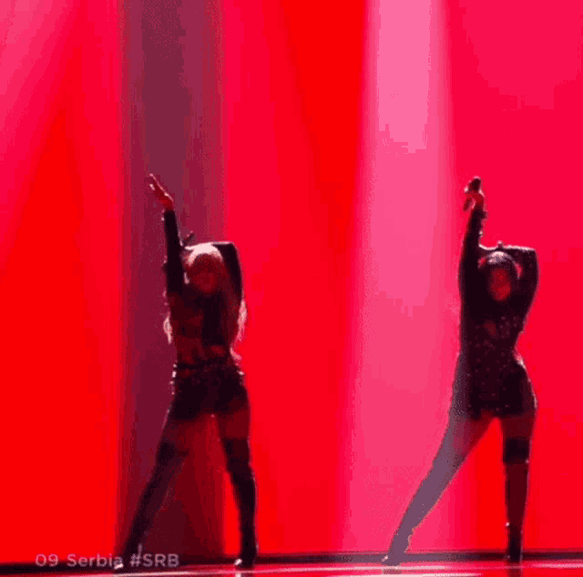 a couple of women are dancing on a stage in front of a red background .