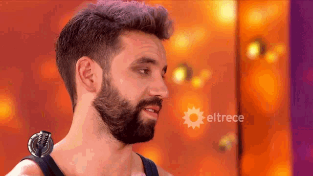 a man with a beard is standing in front of a screen that says eltrece on it