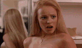 a naked woman is looking at herself in a mirror and making a surprised face .