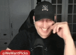 a man wearing a black hat is smiling in front of a microphone with the words we want picks in the corner