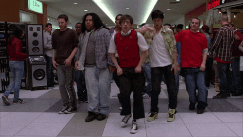 a group of people are dancing in a mall with a sign that says j.crew on it