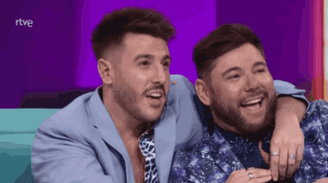 two men are sitting next to each other with a purple background and the word rtve on the bottom